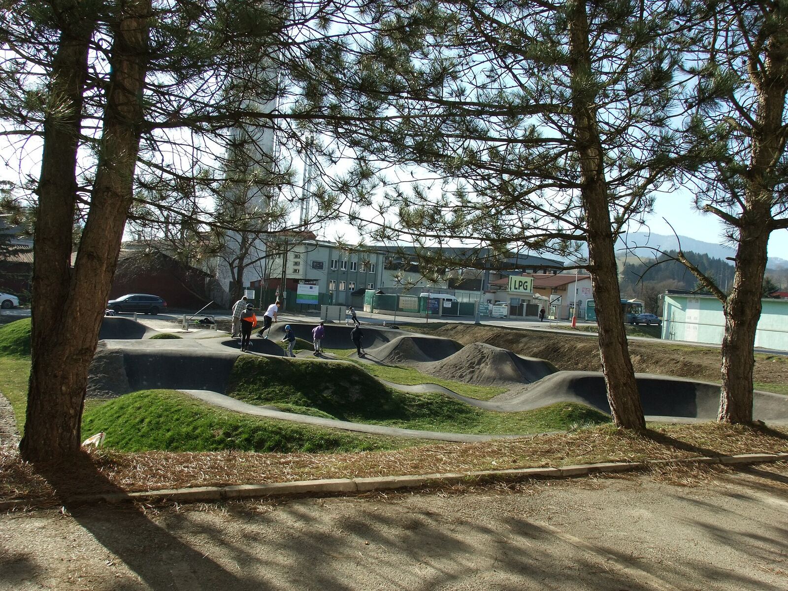 Des jeunes roulent sur un pumptrack de quartier entouré de pins, à Dolný Kubín en Slovaquie
